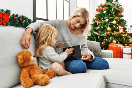 Foto de Madre e hija leyendo libro sentado junto al árbol de navidad en casa - Imagen libre de derechos