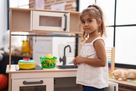 Téléchargez les photos : Adorable fille hispanique jouant avec la cuisine de jeu debout à la maternelle - en image libre de droit