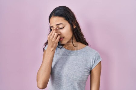 Foto de Young brazilian woman wearing casual t shirt over pink background tired rubbing nose and eyes feeling fatigue and headache. stress and frustration concept. - Imagen libre de derechos