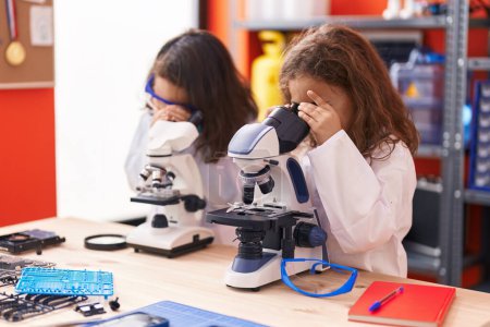Foto de Dos niños estudiantes usando microscopios de pie en el aula de laboratorio - Imagen libre de derechos