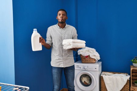 Photo for African american man holding clean towels making fish face with mouth and squinting eyes, crazy and comical. - Royalty Free Image