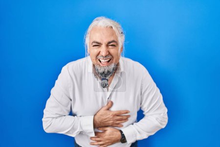 Téléchargez les photos : Middle age man with grey hair standing over blue background smiling and laughing hard out loud because funny crazy joke with hands on body. - en image libre de droit