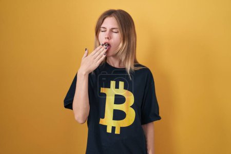 Téléchargez les photos : Blonde caucasian woman wearing bitcoin t shirt bored yawning tired covering mouth with hand. restless and sleepiness. - en image libre de droit