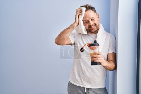 Téléchargez les photos : Jeune homme caucasien boire une boisson protéinée en utilisant une serviette au centre sportif - en image libre de droit
