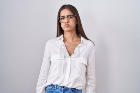 Foto de Young brunette woman wearing glasses puffing cheeks with funny face. mouth inflated with air, crazy expression. - Imagen libre de derechos