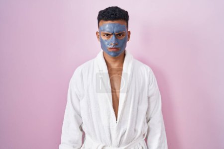 Photo for Young hispanic man wearing beauty face mask and bath robe skeptic and nervous, frowning upset because of problem. negative person. - Royalty Free Image