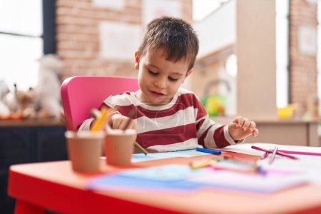 Photo for Adorable toddler student drawing on notebook sitting on table at kindergarten - Royalty Free Image