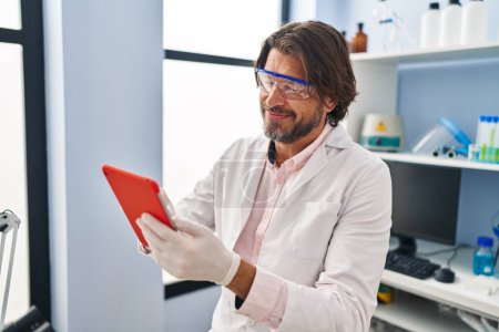 Foto de Hombre científico de mediana edad sonriendo confiado usando touchpad en el laboratorio - Imagen libre de derechos