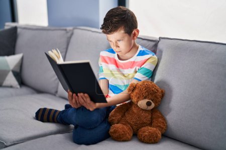 Photo for Young caucasian kid sitting on the sofa reading a book skeptic and nervous, frowning upset because of problem. negative person. - Royalty Free Image