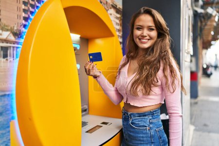 Photo for Young hispanic woman taking cash from atm with credit card looking positive and happy standing and smiling with a confident smile showing teeth - Royalty Free Image