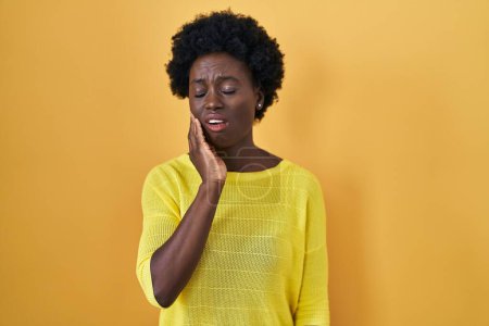 Foto de Mujer joven africana de pie sobre el estudio amarillo tocando la boca con la mano con expresión dolorosa debido a dolor de muelas o enfermedad dental en los dientes. dentista - Imagen libre de derechos