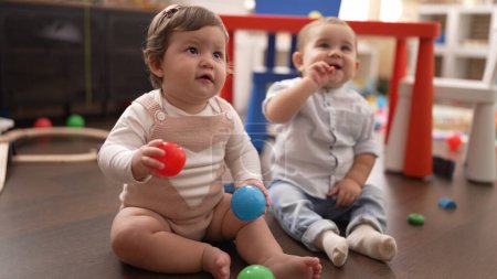 Foto de Dos niños pequeños jugando con bolas sentados en el suelo en el jardín de infantes - Imagen libre de derechos