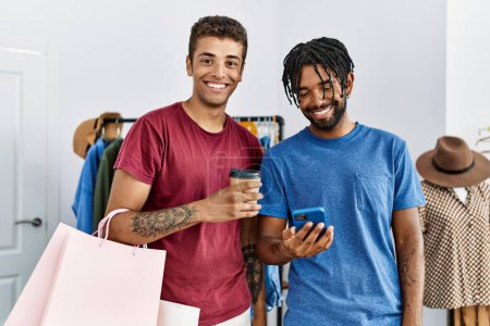 Photo for Two men friends holding shopping bags using smartphone at clothing store - Royalty Free Image
