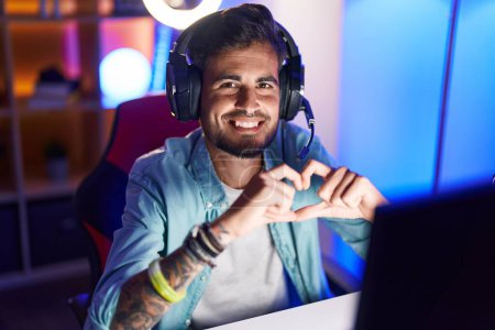 Téléchargez les photos : Young hispanic man streamer smiling confident doing heart symbol with hands at gaming room - en image libre de droit