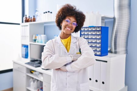 Foto de Young african american woman working at scientist laboratory happy face smiling with crossed arms looking at the camera. positive person. - Imagen libre de derechos