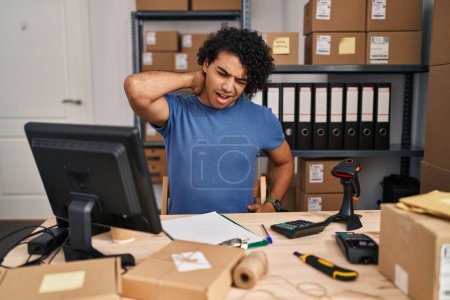 Foto de Hombre hispano con el pelo rizado que trabaja en el comercio electrónico de la pequeña empresa que sufre de lesión del dolor de cuello, tocando el cuello con la mano, dolor muscular - Imagen libre de derechos