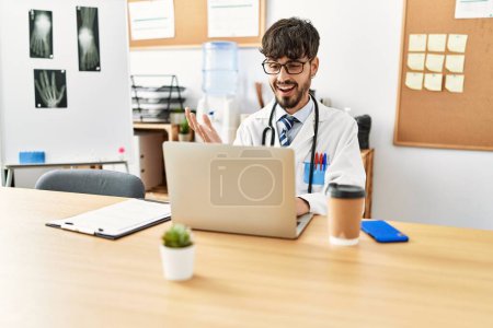 Photo for Young hispanic doctor man having video call using laptop at clinic - Royalty Free Image