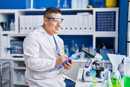 Photo for Young latin man scientist writing report working at laboratory - Royalty Free Image