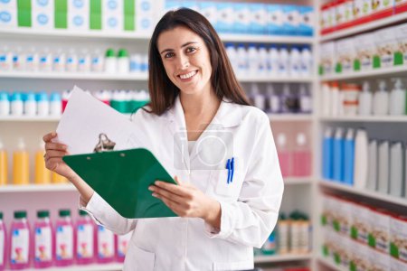 Photo for Young beautiful hispanic woman pharmacist reading document standing at pharmacy - Royalty Free Image