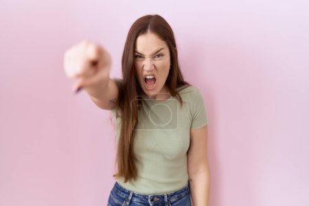Téléchargez les photos : Belle femme brune debout sur fond rose pointant mécontent et frustré à la caméra, en colère et furieux contre vous - en image libre de droit