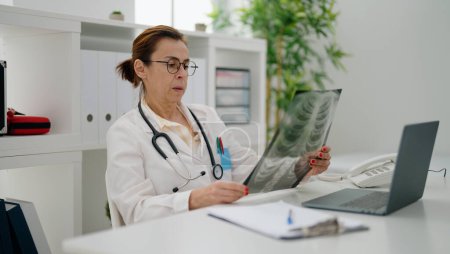 Foto de Mujer hispana de mediana edad vistiendo uniforme médico mirando rayos X en la clínica - Imagen libre de derechos