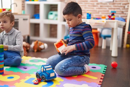 Foto de Dos niños jugando con bloques de construcción y juguete de camión sentado en el suelo en el jardín de infantes - Imagen libre de derechos