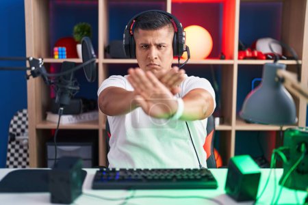 Téléchargez les photos : Jeune homme hispanique jouant à des jeux vidéo expression de rejet croisement des bras et des paumes faisant signe négatif, visage en colère - en image libre de droit