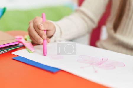 Foto de Adorable niña hispana preescolar sentada en la mesa dibujando en papel en el jardín de infantes - Imagen libre de derechos