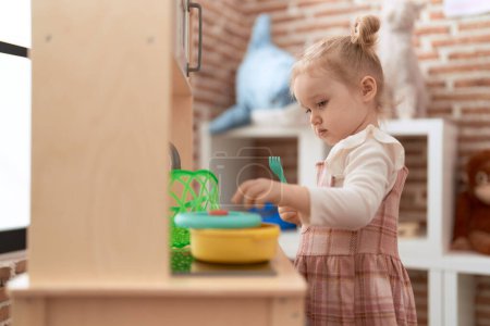 Téléchargez les photos : Adorable fille caucasienne jouer avec jouer cuisine debout à la maternelle - en image libre de droit