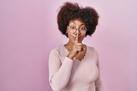Photo for Young african american woman standing over pink background asking to be quiet with finger on lips. silence and secret concept. - Royalty Free Image
