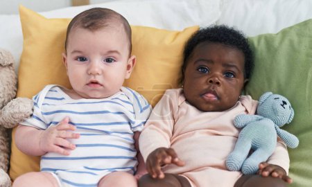 Téléchargez les photos : Deux adorables bébés assis sur le lit dans la chambre - en image libre de droit