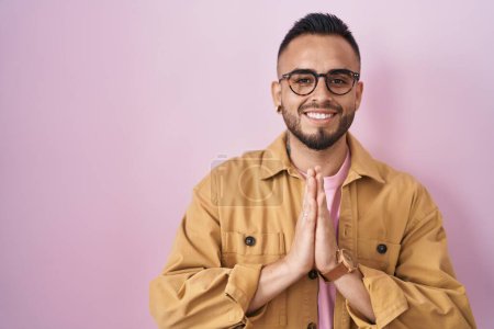 Téléchargez les photos : Jeune homme hispanique debout sur fond rose priant avec les mains ensemble demandant pardon souriant confiant. - en image libre de droit