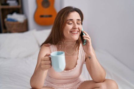 Téléchargez les photos : Young woman talking on smartphone drinking coffee at bedroom - en image libre de droit