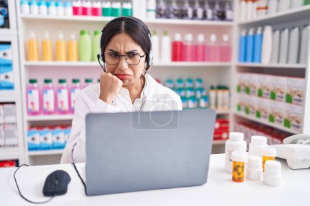 Foto de Mujer árabe joven que trabaja en la farmacia usando una computadora portátil que parece estresada y nerviosa con las manos en la boca mordiéndose las uñas. problema de ansiedad. - Imagen libre de derechos
