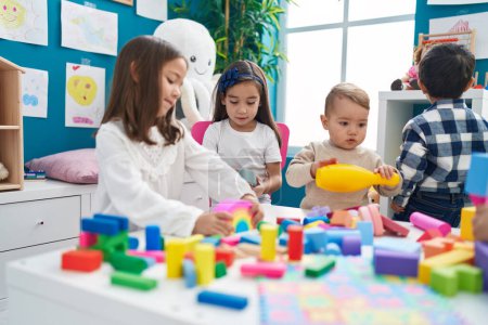 Foto de Grupo de niños jugando con bloques de construcción sentados en la mesa en el jardín de infantes - Imagen libre de derechos