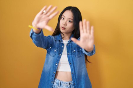 Foto de Young asian woman standing over yellow background doing frame using hands palms and fingers, camera perspective - Imagen libre de derechos