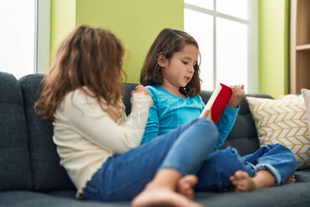 Photo for Two kids reading book sitting on sofa at home - Royalty Free Image