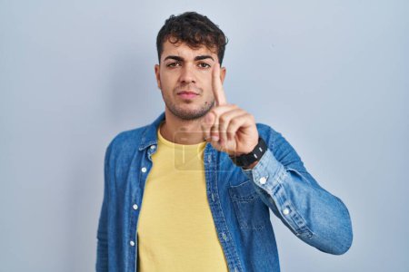 Téléchargez les photos : Jeune homme hispanique debout sur fond bleu pointant du doigt et l'expression en colère, ne montrant aucun geste - en image libre de droit