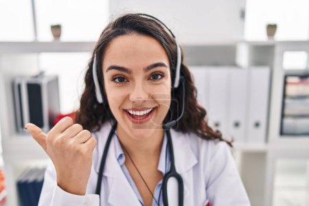 Photo for Young doctor woman working on online appointment pointing thumb up to the side smiling happy with open mouth - Royalty Free Image