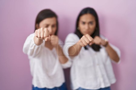 Foto de Hispanic mother and daughter together punching fist to fight, aggressive and angry attack, threat and violence - Imagen libre de derechos