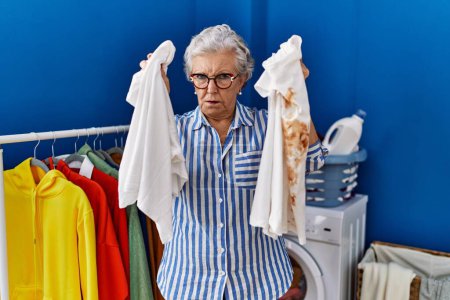 Photo for Senior woman with grey hair holding clean white t shirt and t shirt with dirty stain depressed and worry for distress, crying angry and afraid. sad expression. - Royalty Free Image