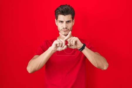 Photo for Young hispanic man standing over red background rejection expression crossing fingers doing negative sign - Royalty Free Image