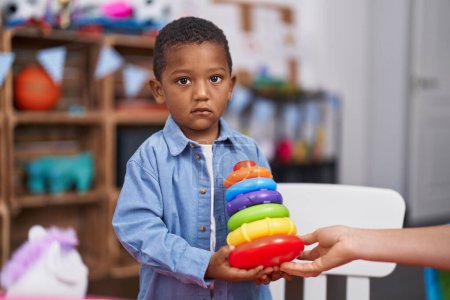 Foto de Niño afroamericano sosteniendo torre de plástico de aros juguete de pie en el jardín de infantes - Imagen libre de derechos