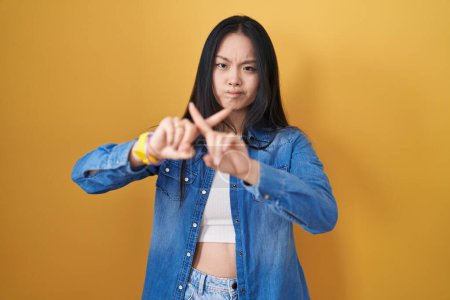 Téléchargez les photos : Jeune femme asiatique debout sur fond jaune rejet expression croisement doigts faire signe négatif - en image libre de droit