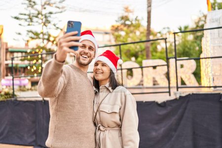 Foto de Hombre y mujer pareja con sombrero de Navidad hacen selfie por el teléfono inteligente en el parque - Imagen libre de derechos