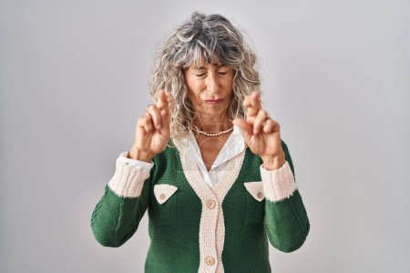 Téléchargez les photos : Middle age woman standing over white background gesturing finger crossed smiling with hope and eyes closed. luck and superstitious concept. - en image libre de droit