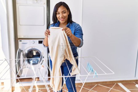 Photo for Hispanic brunette woman hanging clean laundry on rack at laundry room - Royalty Free Image