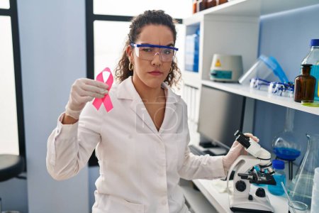 Téléchargez les photos : Jeune femme hispanique travaillant dans un laboratoire scientifique à la recherche d'un remède contre le cancer du sein sceptique et nerveux, fronçant les sourcils bouleversés à cause d'un problème. personne négative. - en image libre de droit