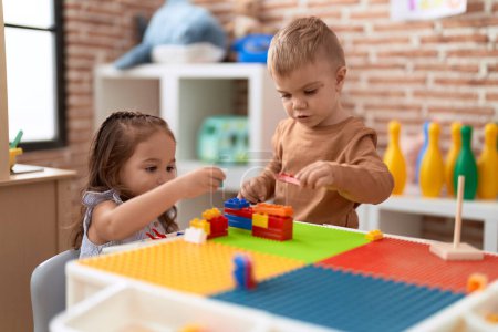 Foto de Adorable chica y niño jugando con piezas de bloques de construcción sentado en la mesa en el jardín de infantes - Imagen libre de derechos