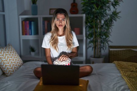 Téléchargez les photos : Young blonde woman sitting on the bed at home watching a movie from laptop depressed and worry for distress, crying angry and afraid. sad expression. - en image libre de droit